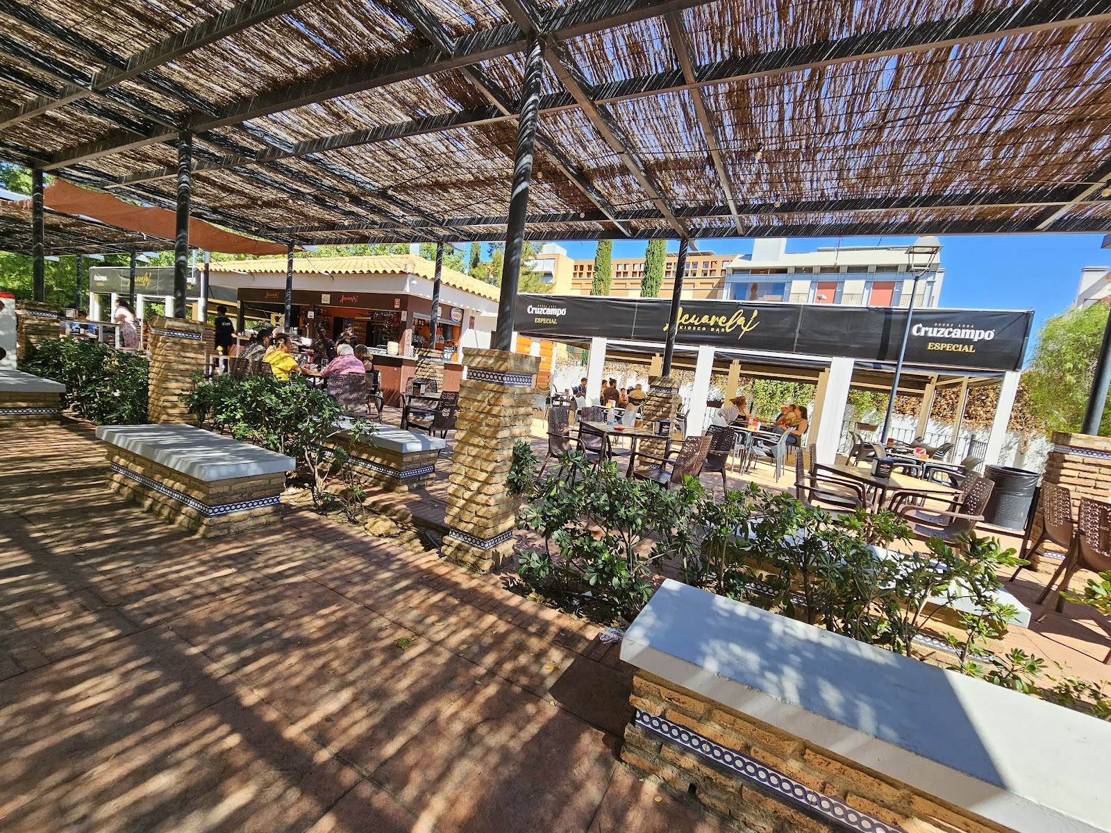 Terraza de Acuarela Kiosco Bar, rodeada de plantas y mesas bajo una pérgola